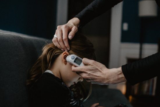 Mother taking the temperature of her daughter with an ear thermometer